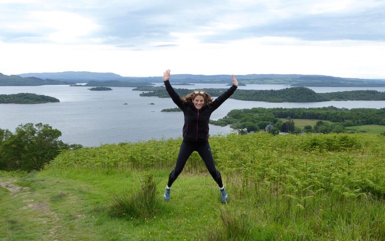 a woman doing a starjump on a guided hike around loch lomond